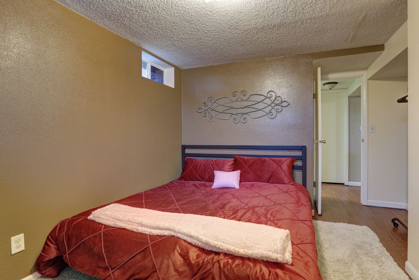 A bedroom with a bed, a decorative wall piece, a window, and a door.