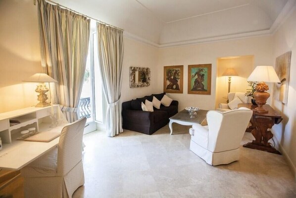 A well-lit living room with a sofa, armchairs, a coffee table, and a desk with a lamp. - Relais Corte Degli Aragonesi (Ischia)