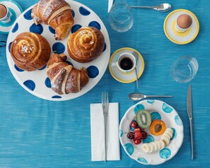 A breakfast setting with croissants, a fruit plate, coffee, and a glass of water on a blue tablecloth. - Relais Corte Degli Aragonesi (Ischia)