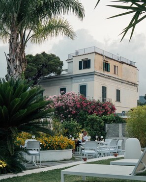 A two-story building with a balcony, surrounded by lush greenery and flowering plants. - Relais Corte Degli Aragonesi (Ischia)