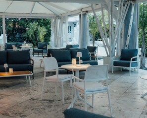 An outdoor seating area with white chairs and dark green sofas under a white canopy, surrounded by greenery. - Relais Corte Degli Aragonesi (Ischia)