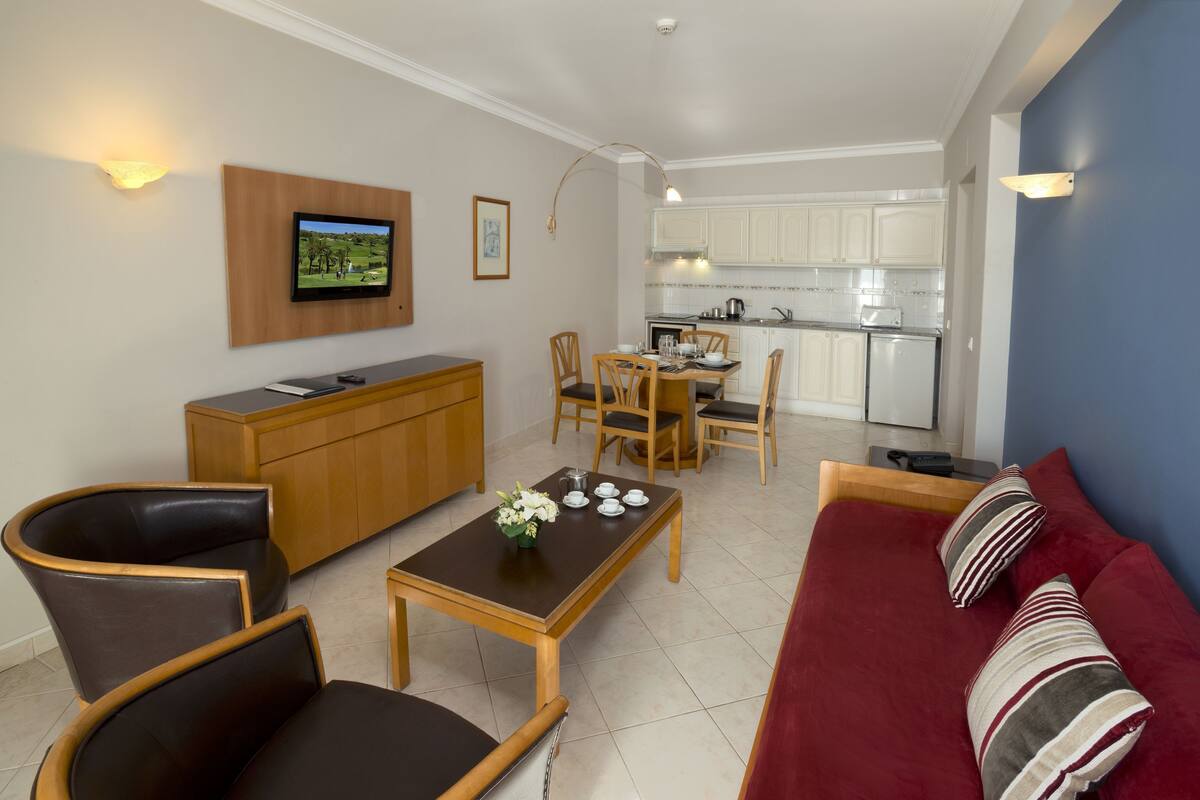 Uma sala de estar com televisão, móveis de madeira, área de jantar e cozinha.