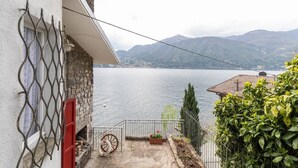 Un edificio de piedra con puerta roja, una valla de metal y vistas a un lago con montañas al fondo.