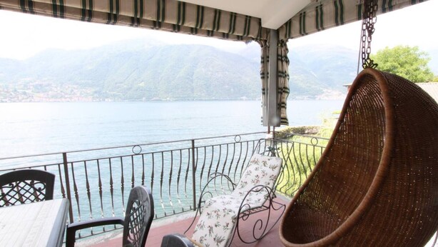 Un balcón con una silla colgante, una butaca con cojín y una mesa, con vistas a un lago y montañas.