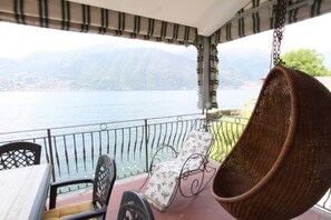 Un balcón con una silla colgante, una butaca con cojín y una mesa, con vistas a un lago y montañas.