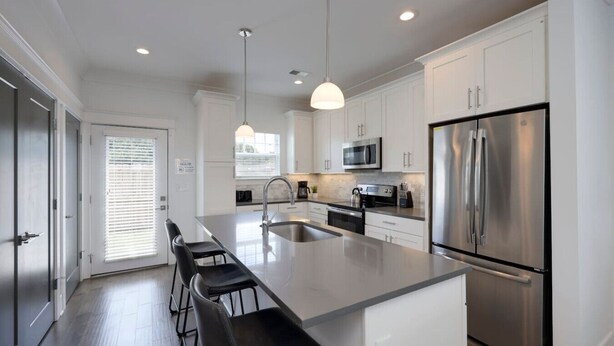 A modern kitchen with white cabinetry, stainless steel appliances, and a central island with bar stools.