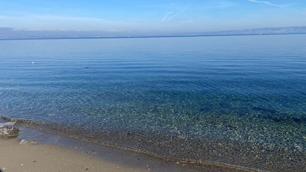 Ein klarer Blick auf einen Strand mit ruhigem Wasser und einer entfernten Küste.