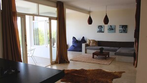 A living room with a sofa, a coffee table, and a rug. There is a glass door leading outside. - Toca do Sol com vista natureza em Pipa (Tibau do Sul)