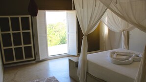 A bedroom with a bed, a window with curtains, a view of greenery outside, and a patterned rug. - Toca do Sol com vista natureza em Pipa (Tibau do Sul)