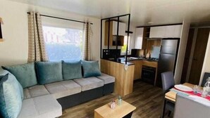 A compact living space with a sofa, a small table, a kitchenette, and a dining area. - Mobile home from 2022 at La Carabasse campsite (Vias)