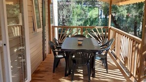 A covered patio with a wooden table and chairs, surrounded by a wooden railing. - Mobile home from 2022 at La Carabasse campsite (Vias)