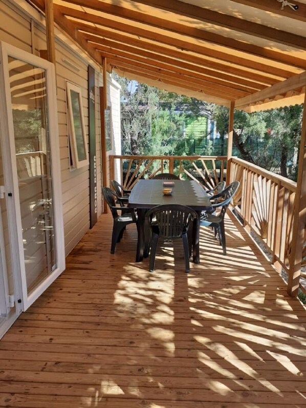 Une terrasse couverte avec une table et des chaises en bois, entourée d’une balustrade en bois.