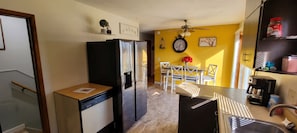 A compact kitchen with a dishwasher, refrigerator, dining table with chairs, and a coffee machine.