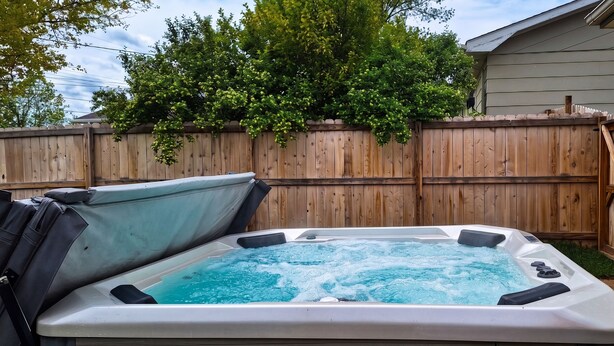 A hot tub in a backyard with a wooden fence and a house in the background.