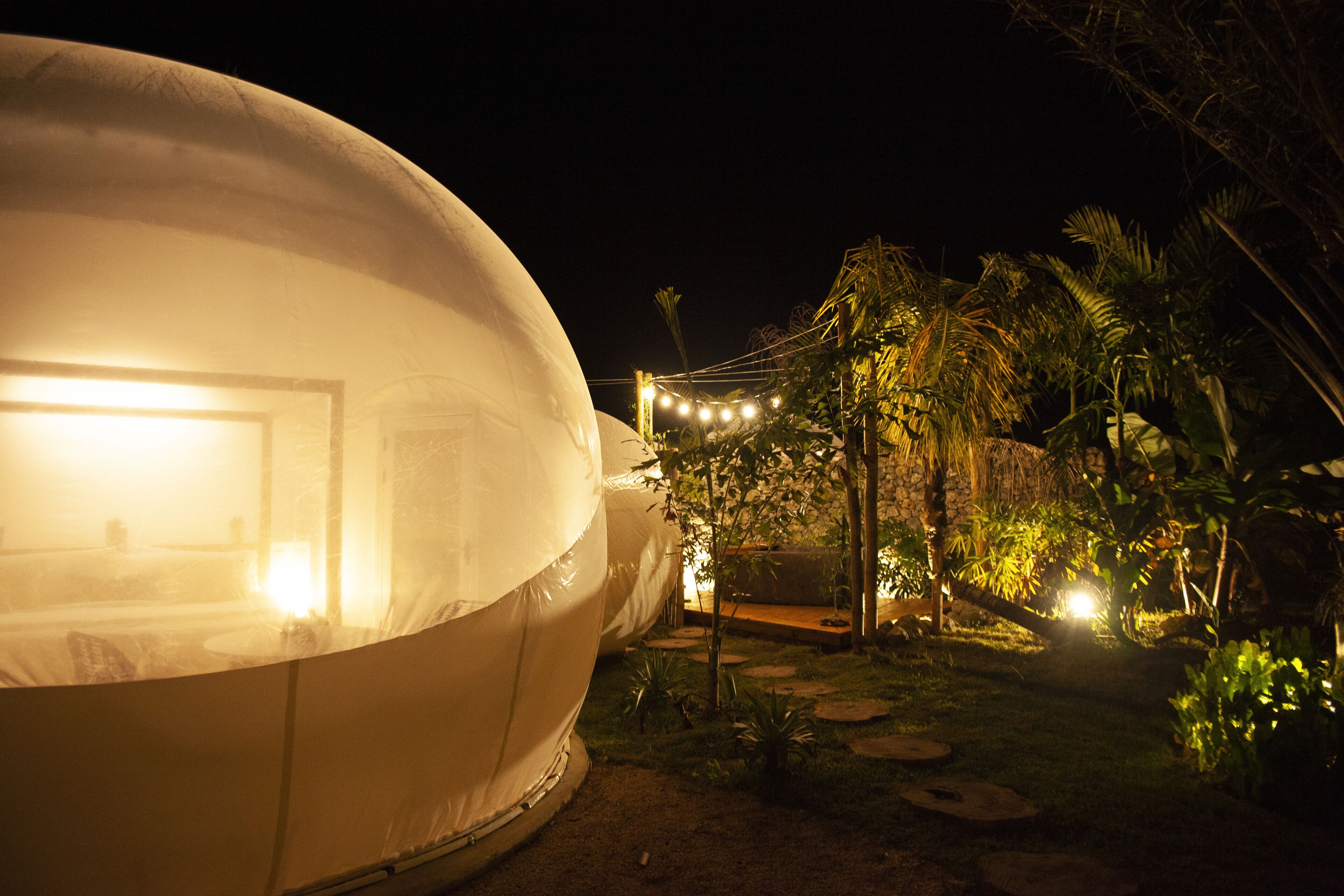 A large dome-shaped structure with a visible entrance, surrounded by a garden with palm trees and a string of lights.