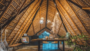 Un intérieur doté d’un toit de chaume, d’une table en bois avec des chaises et de plantes suspendues.