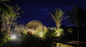 Un edificio de forma abovedada con una entrada circular, rodeado de abundante vegetación y palmeras.