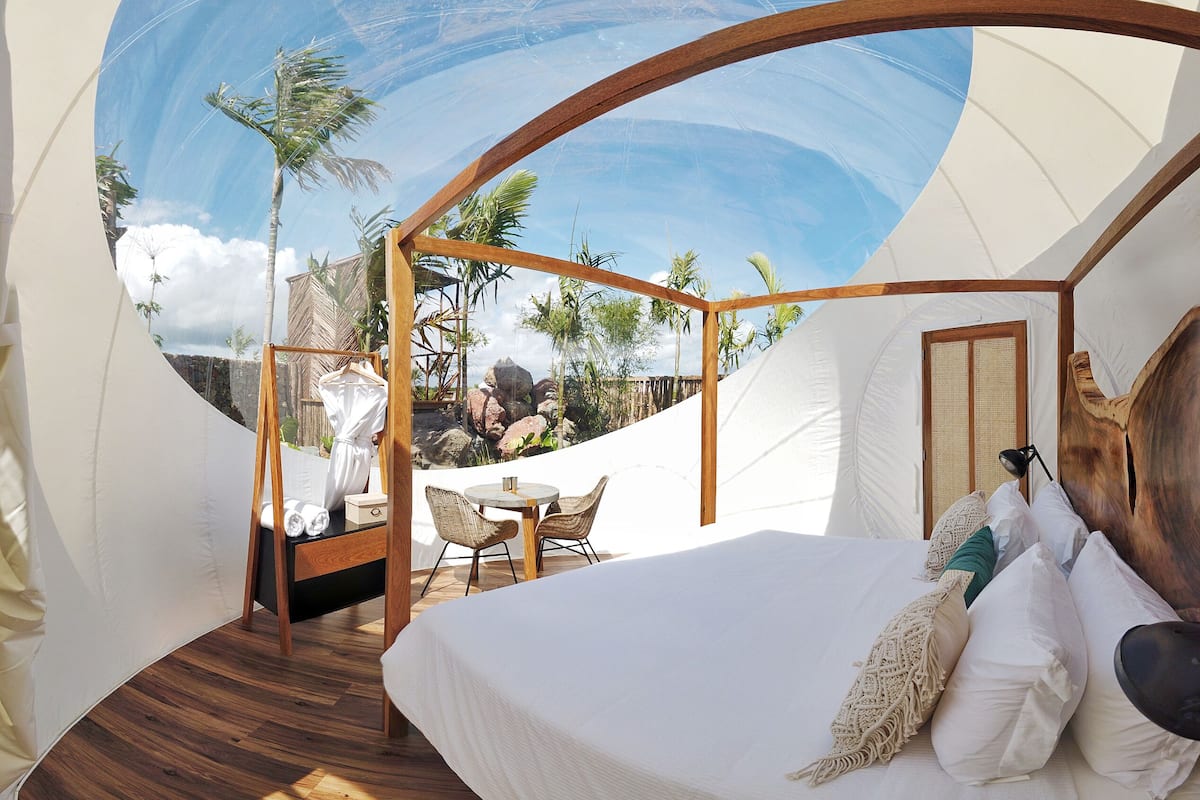 Een tentaccomodatie met een bed, een tafeltje, stoelen en uitzicht op palmbomen.