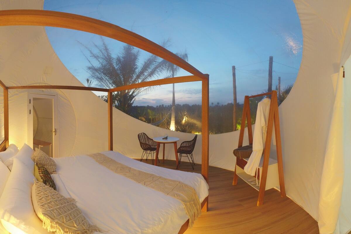 Een slaapkamer met een bed, een tafeltje, twee stoelen en uitzicht op palmbomen.