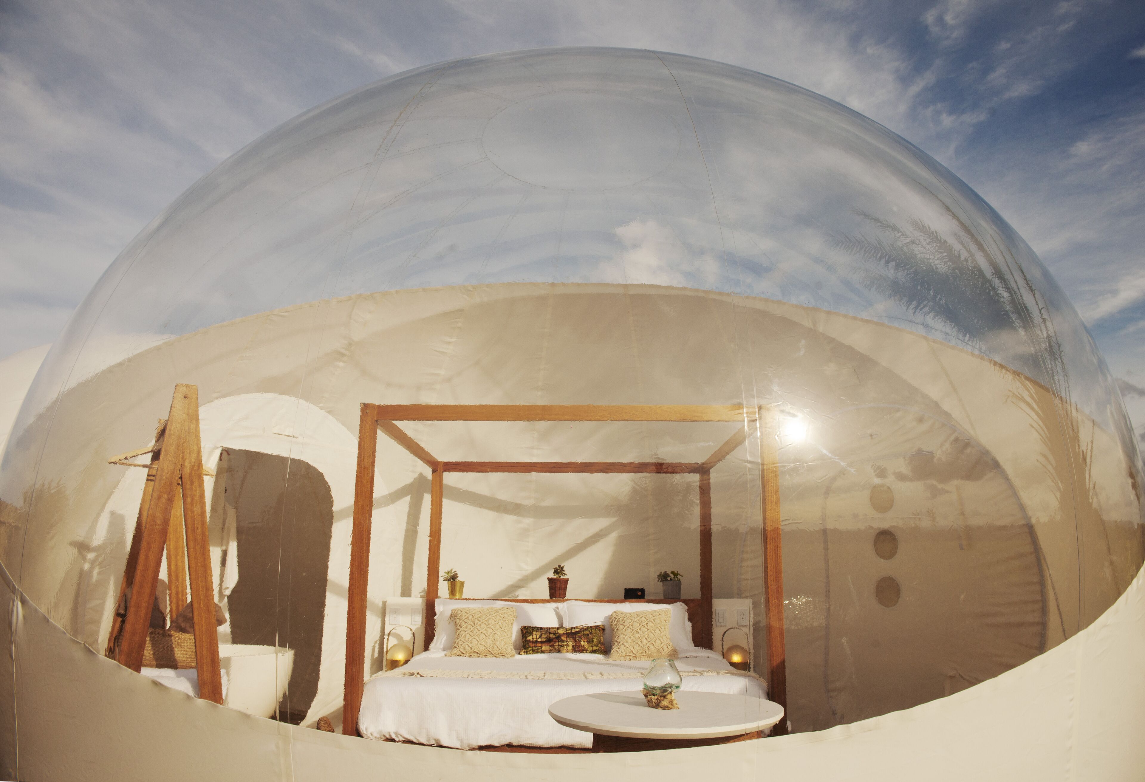 Una habitación con forma de cúpula transparente, con cama, mesita de noche y una pequeña mesa redonda.