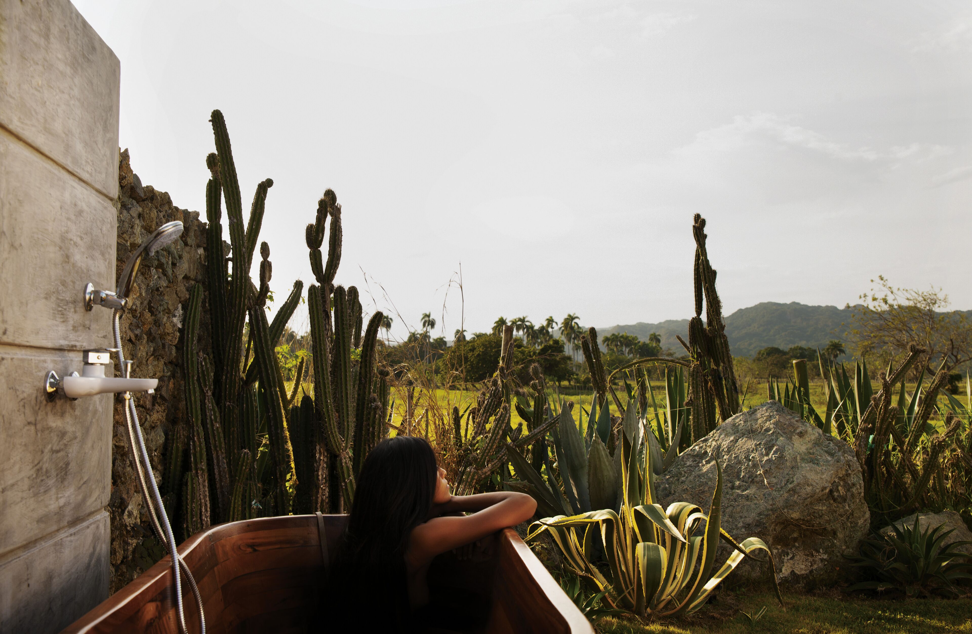 A bathtub with a view of a desert landscape, including cacti and distant hills.