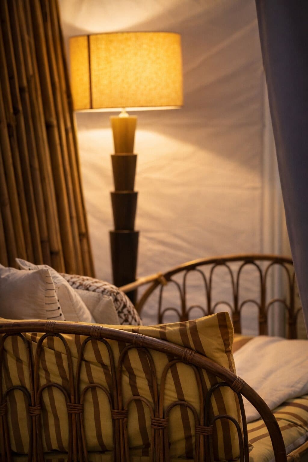 A room with a bed, a nightstand with a lamp, and a wicker chair.