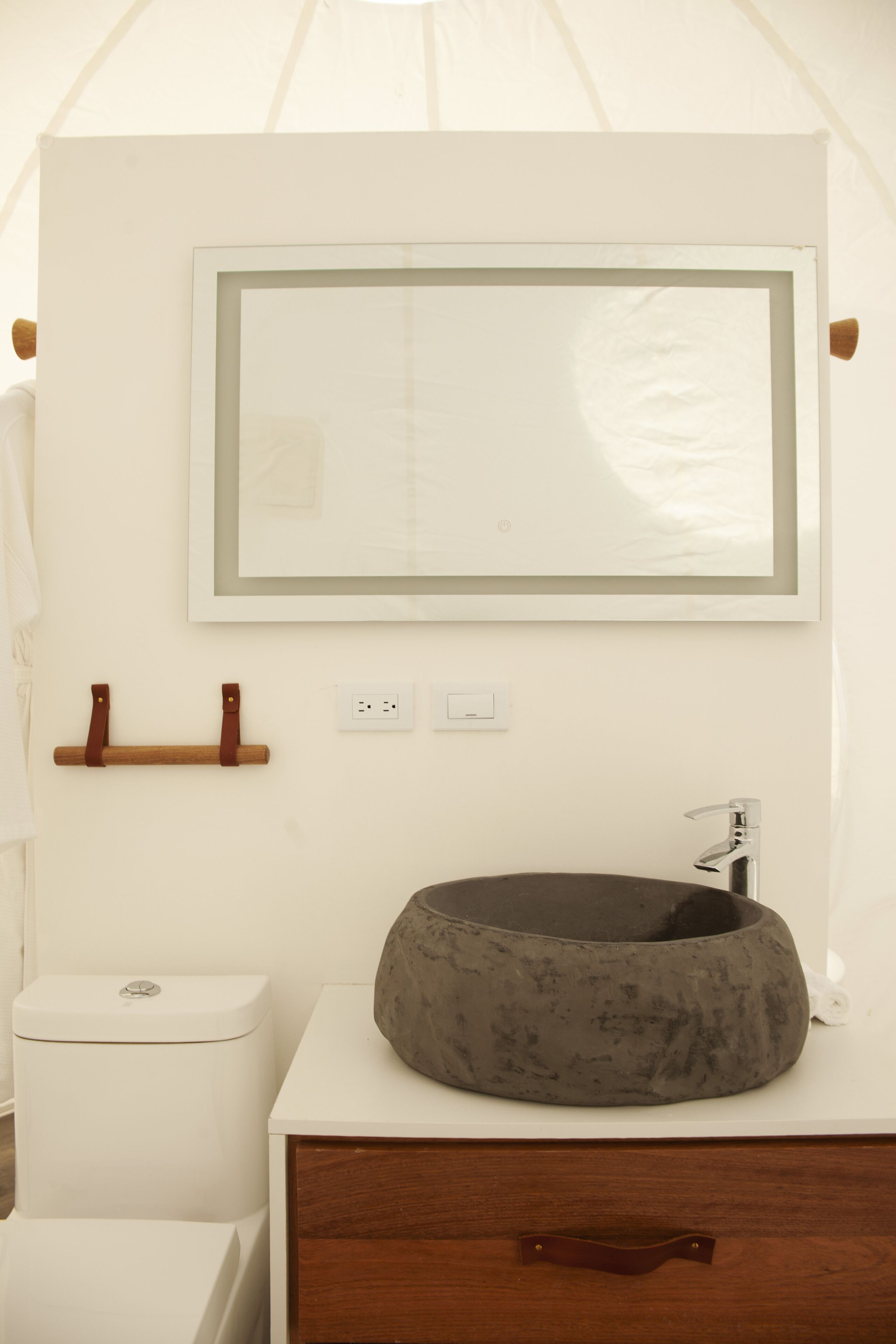 Ein Badezimmer mit Toilette, rundem Waschbecken mit dunkler Schüssel, Holzhandtuchhalter und einem gerahmten Spiegel an der Wand.