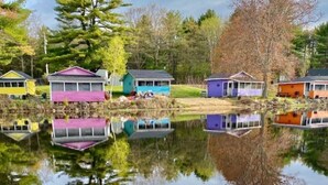A row of colorful houses by a calm lake with reflections, surrounded by trees and greenery. - Lakefront Pink Cottage (Northwood)