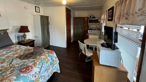 A compact room with a bed, a desk, a chair, a television, and a kitchenette. - Lakefront Pink Cottage (Northwood)