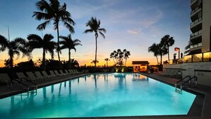 Piscina com espreguiçadeiras e palmeiras ao pôr do sol.