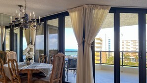 Espaço de refeições com mesa, cadeiras e um candelabro. Dá-se vista para uma varanda com cortina.