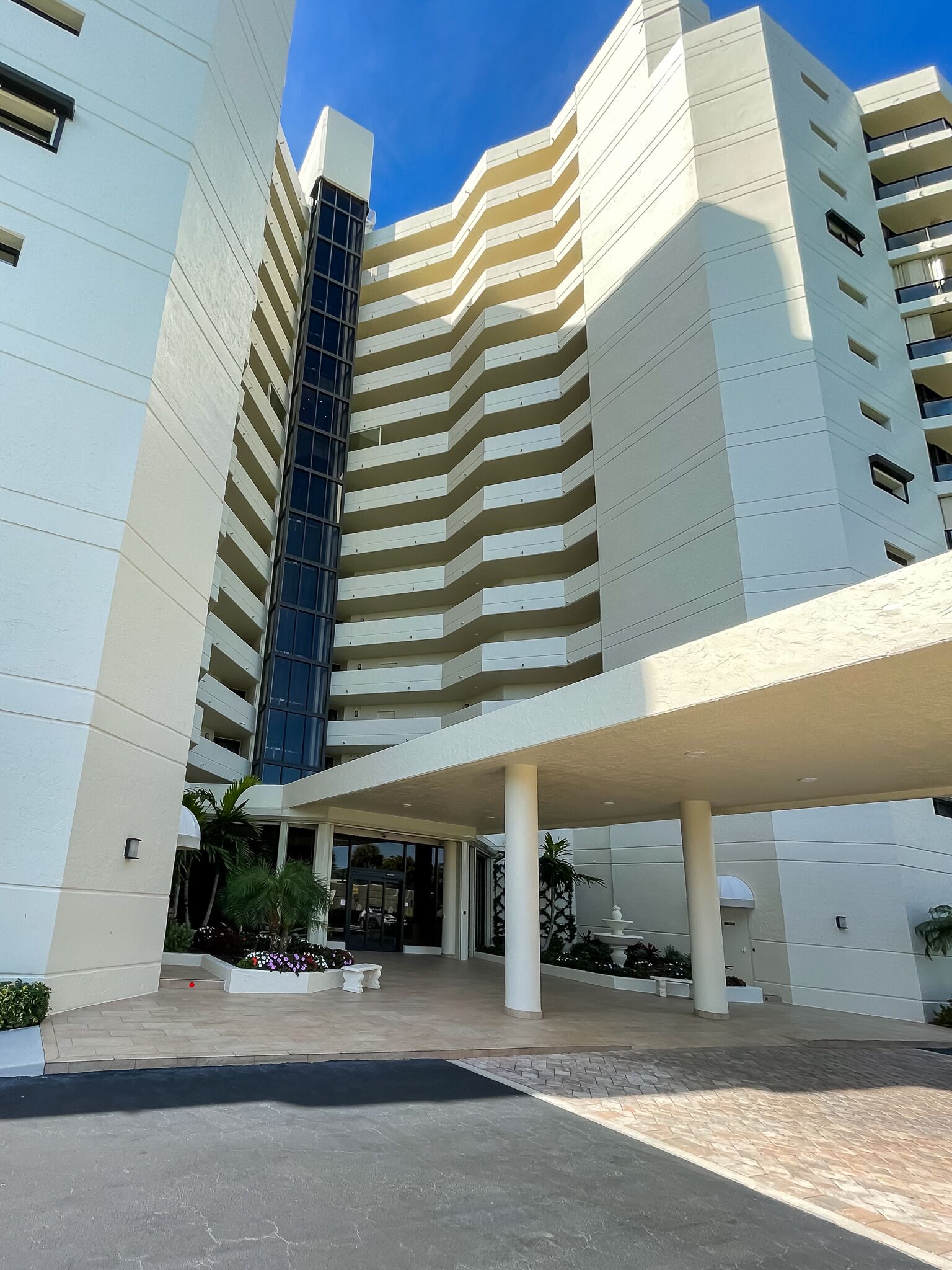 Un hotel moderno con una entrada destacada, varios pisos y un espacio al aire libre cubierto con asientos.
