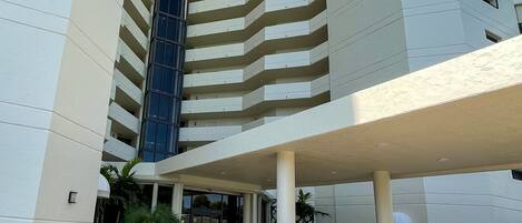 Un hotel moderno con una entrada destacada, varios pisos y un espacio al aire libre cubierto con asientos.
