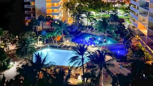 Um hotel com vários andares, piscina e palmeiras.
