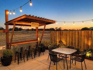 An outdoor patio with a pergola labeled 'Brewing Station,' surrounded by chairs and a table, with string lights overhead. - Russian River Brew-cation Home (Santa Rosa)