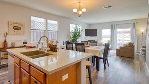 A modern kitchen with a central island, dining area with chairs, a sofa, and a TV in the background. - Russian River Brew-cation Home (Santa Rosa)
