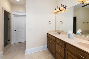 Un baño con lavamanos doble, tocador de madera y un espejo grande con luces empotradas.