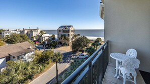A balcony with white metal chairs and a table overlooking a residential area with a beach view. - Sea Point Condo #302 (Saint Simons Island)