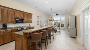 A spacious kitchen with wooden cabinets, a central island with bar stools, a large window, and a ceiling fan. - Sea Point Condo #302 (Saint Simons Island)