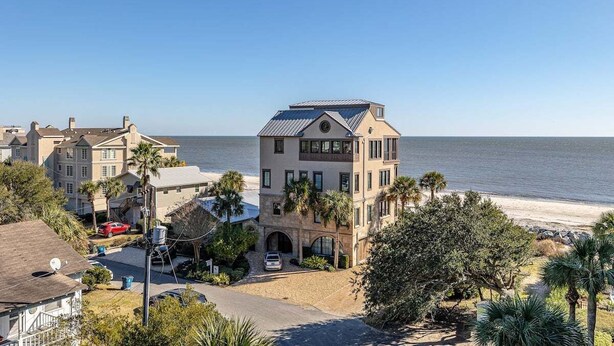 A coastal residential area with a prominent two-story house featuring a solar panel roof, a driveway, and a view of the beach. - Sea Point Condo #302 (Saint Simons Island)