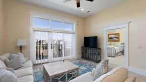 A living room with a sofa set, a coffee table, a television, and a large window with blinds. - Sea Point Condo #302 (Saint Simons Island)