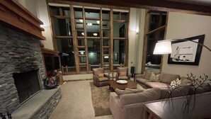 A cozy living room with a stone fireplace, leather sofas, a coffee table, and large windows. - Luxury ski-in townhome in Solitude Resort (Salt Lake City)