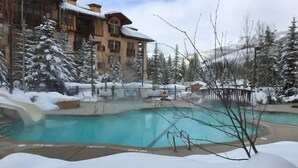 A pool area with a snow-covered landscape, a building with multiple windows, and a clear sky. - Luxury ski-in townhome in Solitude Resort (Salt Lake City)