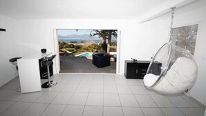 Un saló modern amb una cadira penjant, una zona de bar i vistes a una piscina i muntanyes.