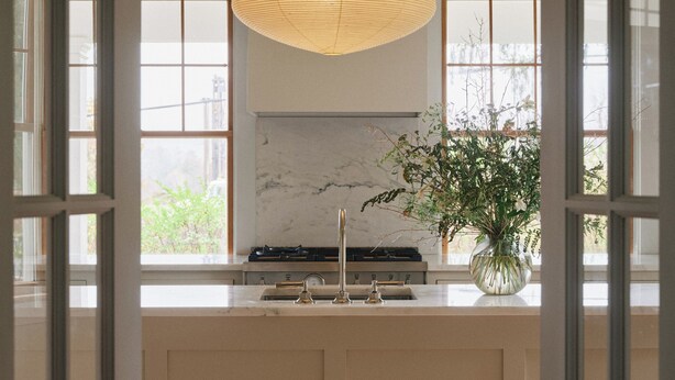 A modern kitchen with a central island, pendant light, and a view of greenery outside.