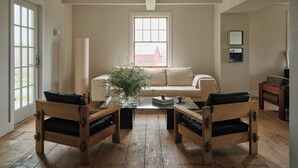 A living room with a wooden floor, a sofa, two armchairs, a coffee table, and a window with a view of a building.