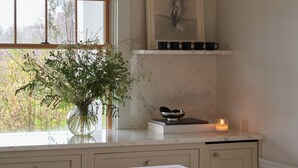 A kitchen with a marble countertop, a vase with greenery, a candle, and a framed artwork above the counter.