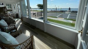 A room with large windows overlooking a waterfront area, including a parking lot and a pedestrian path. - Ocean front and 3 beaches across,parks, short walk to historic downtown! (Gloucester)
