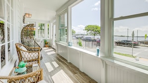 A bright, sunlit room with large windows, wicker furniture, and a view of a street and water. - Ocean front and 3 beaches across,parks, short walk to historic downtown! (Gloucester)