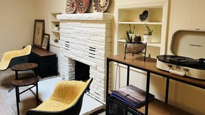 A living room with a white brick fireplace, a black chair, a small table, and a record player.